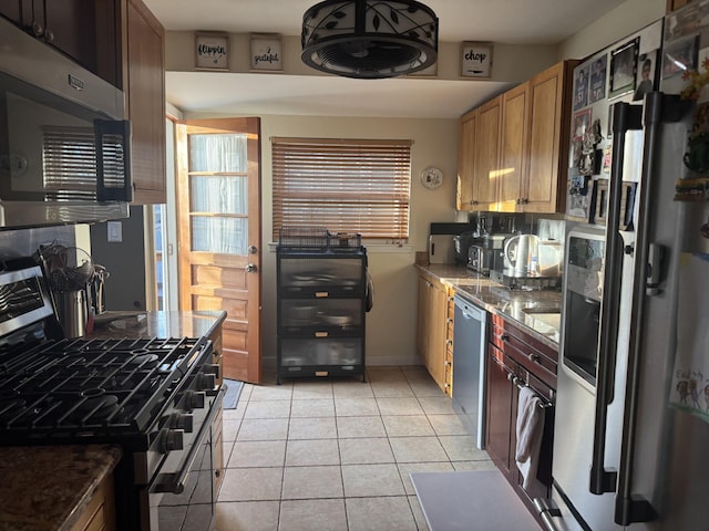 kitchen with appliances with stainless steel finishes, dark stone countertops, and light tile patterned floors