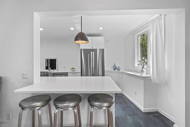 kitchen with freestanding refrigerator, baseboards, a breakfast bar, light countertops, and white cabinets