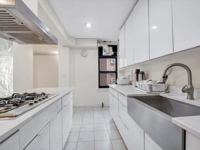 kitchen with a sink, stainless steel gas cooktop, light countertops, white cabinets, and wall chimney exhaust hood