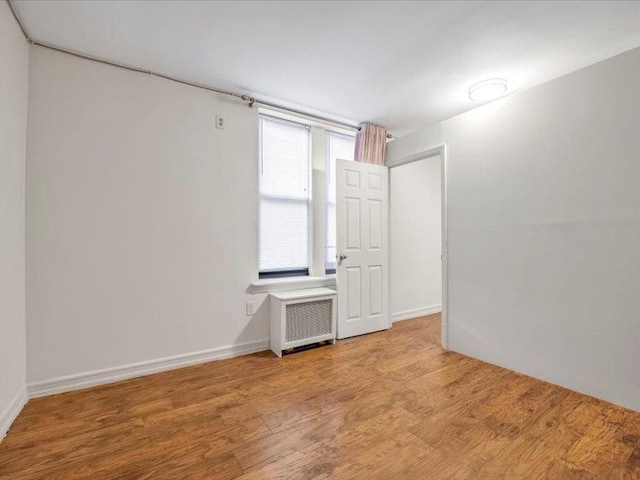 empty room with baseboards, radiator heating unit, and wood finished floors