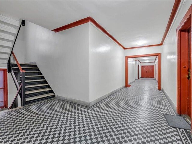 corridor featuring crown molding, baseboards, tile patterned floors, and stairs