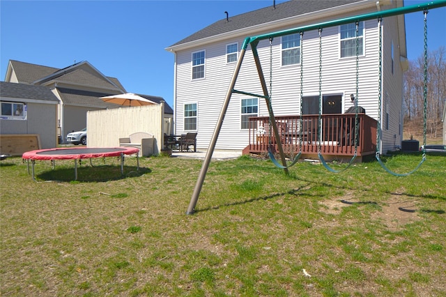rear view of house with a lawn, a deck, central AC unit, and a trampoline