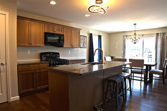 kitchen with a breakfast bar area, a sink, black appliances, an inviting chandelier, and dark stone counters