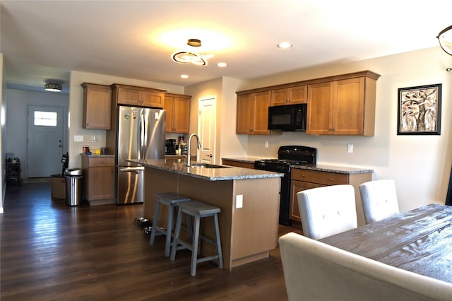kitchen featuring a kitchen bar, a sink, black appliances, dark stone counters, and recessed lighting