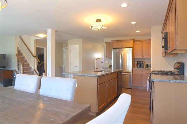 kitchen with light stone countertops, a sink, stainless steel appliances, recessed lighting, and a center island with sink