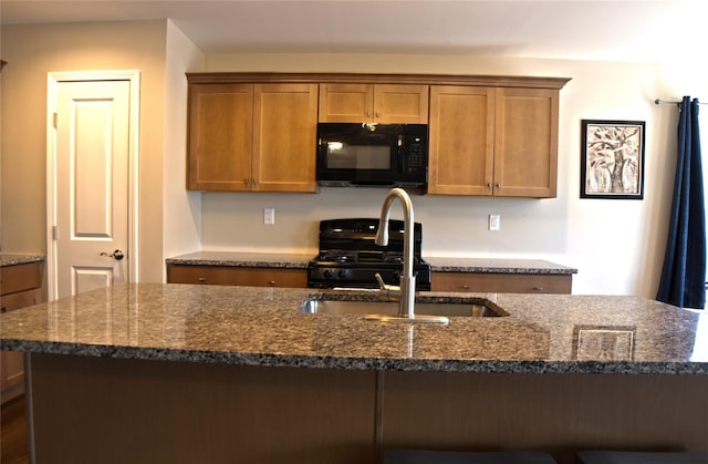 kitchen featuring brown cabinetry, a sink, dark stone counters, and black appliances