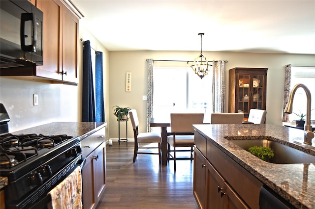 kitchen with an inviting chandelier, dark wood-style flooring, a sink, dark stone countertops, and black appliances
