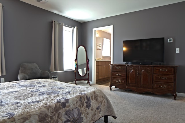 bedroom featuring baseboards, visible vents, ensuite bath, and light colored carpet
