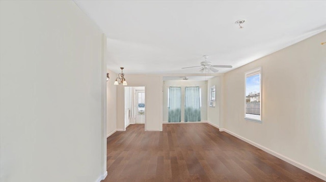 spare room featuring ceiling fan with notable chandelier, wood finished floors, and baseboards