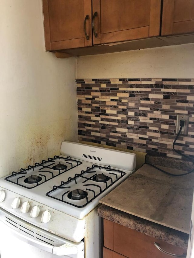 kitchen featuring decorative backsplash, white gas stove, and brown cabinetry