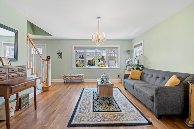 living area featuring baseboards, wood finished floors, stairs, and a notable chandelier