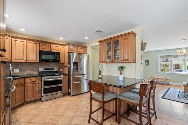 kitchen featuring stainless steel appliances, backsplash, visible vents, a sink, and a notable chandelier