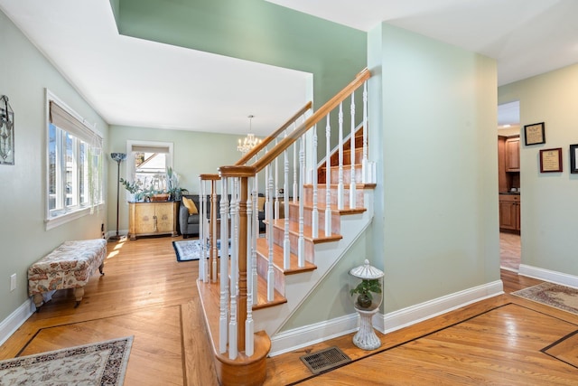 stairway featuring baseboards, wood finished floors, visible vents, and a notable chandelier