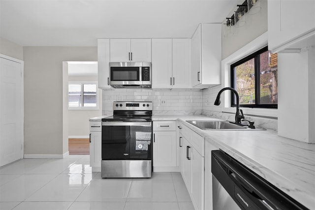 kitchen with a sink, light tile patterned flooring, tasteful backsplash, white cabinetry, and appliances with stainless steel finishes