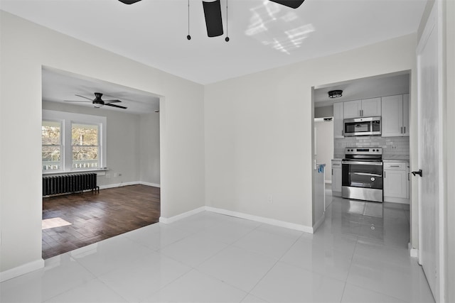 unfurnished living room featuring radiator heating unit, baseboards, ceiling fan, and light tile patterned floors