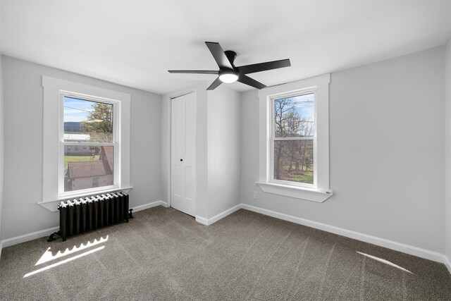 carpeted spare room with radiator, baseboards, a healthy amount of sunlight, and ceiling fan