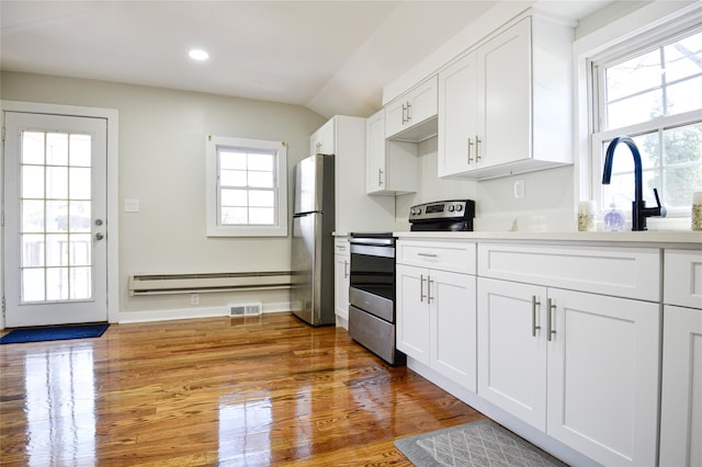 129 Locust Dr, Mastic Beach, NY 11951 - kitchen with stainless steel appliances, a baseboard heating unit, white cabinets, healthy amount of natural light, and recessed lighting