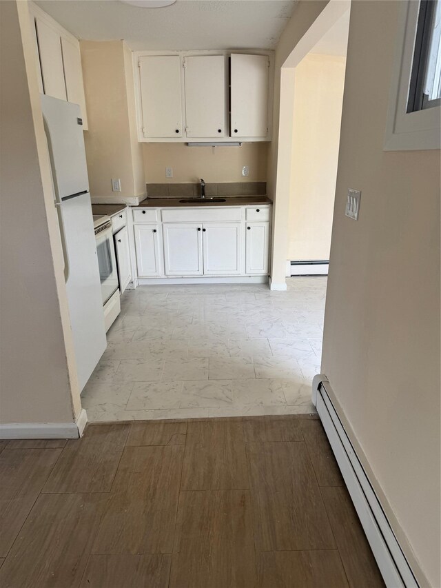 kitchen featuring white appliances, white cabinetry, a sink, and a baseboard radiator