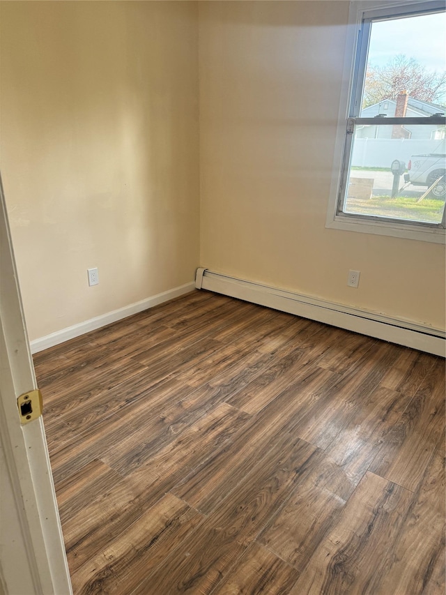 spare room featuring baseboards, a baseboard heating unit, and wood finished floors