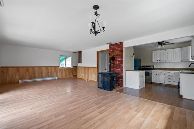 242 Callicoon Center Rd, Jeffersonville, NY 12748 - unfurnished living room featuring wood finished floors, a baseboard radiator, a wainscoted wall, a wood stove, and a ceiling fan