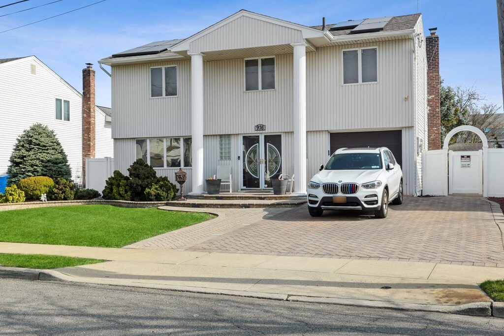 976 Marcel Rd, Baldwin Harbor, NY 11510 - view of front of property featuring solar panels, an attached garage, fence, and decorative driveway
