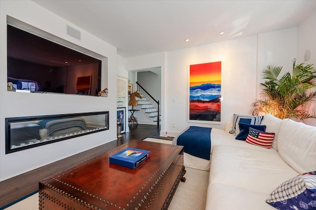 living area with visible vents, a glass covered fireplace, recessed lighting, wood finished floors, and stairway