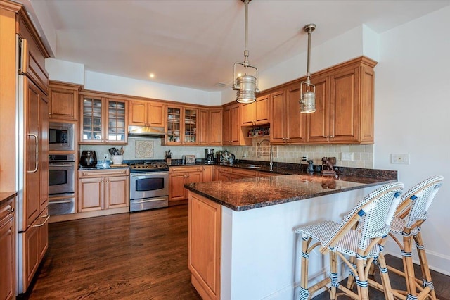 kitchen featuring built in appliances, brown cabinets, a peninsula, and under cabinet range hood