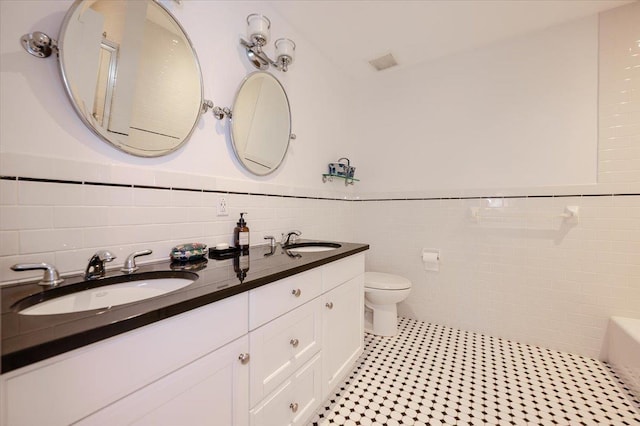 bathroom featuring tile walls, toilet, wainscoting, and a sink