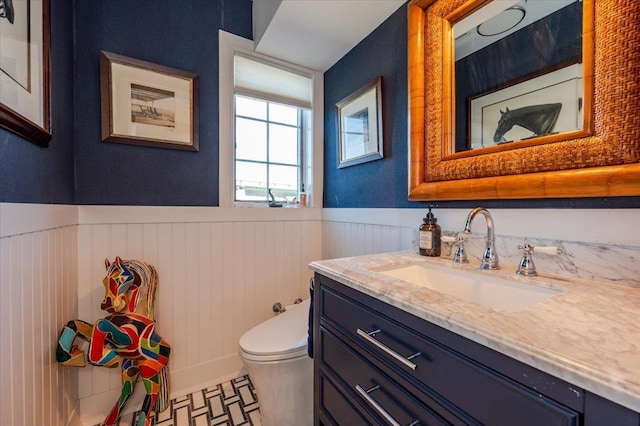 bathroom featuring vanity, toilet, and a wainscoted wall