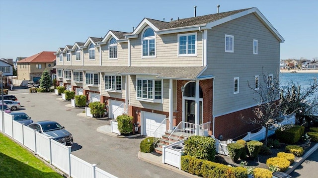 townhome / multi-family property featuring a residential view, driveway, fence, a garage, and brick siding