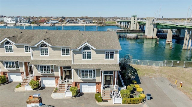 view of front of house with a water view, driveway, fence, an attached garage, and a shingled roof