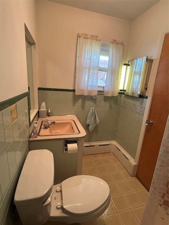 bathroom with tile patterned floors, a wainscoted wall, toilet, a sink, and tile walls