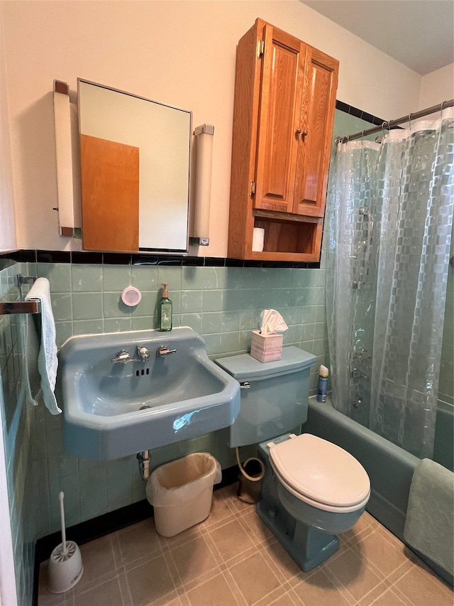 bathroom featuring tile patterned floors, a sink, tile walls, toilet, and shower / bath combo with shower curtain