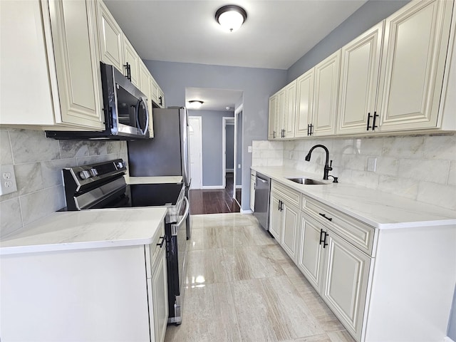 kitchen with a sink, stainless steel appliances, tasteful backsplash, light stone counters, and baseboards