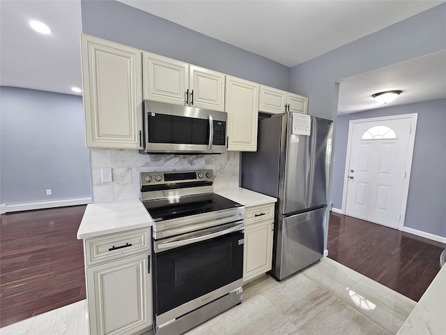 kitchen featuring tasteful backsplash, appliances with stainless steel finishes, light countertops, baseboards, and cream cabinets