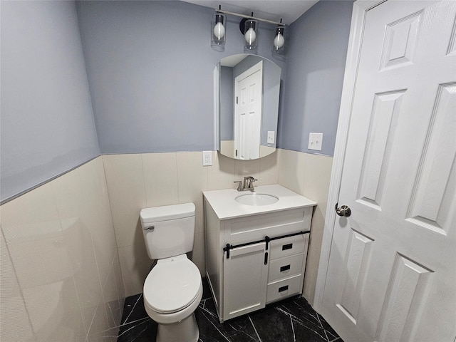 bathroom featuring toilet, marble finish floor, wainscoting, and vanity