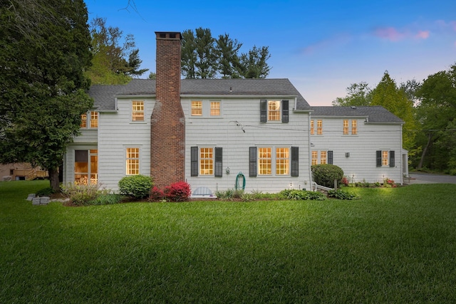 rear view of house featuring a chimney, a yard, and a shingled roof