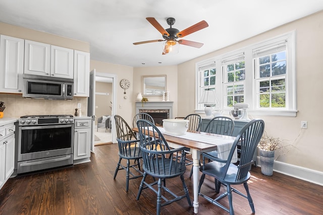 dining space with dark wood-type flooring, a fireplace, ceiling fan, and baseboards