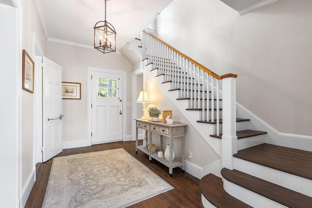 foyer entrance with wood finished floors, stairs, a chandelier, ornamental molding, and baseboards