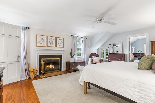 bedroom with wood finished floors, a fireplace with flush hearth, and ceiling fan