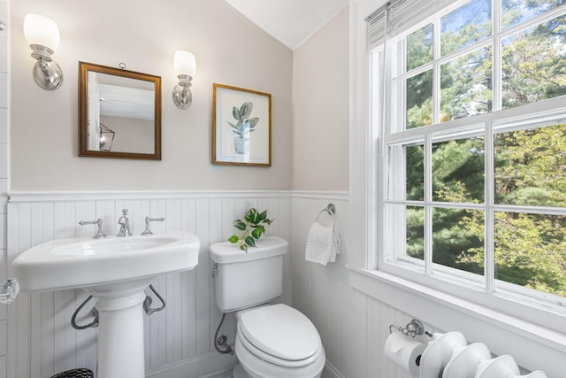 bathroom featuring toilet, vaulted ceiling, healthy amount of natural light, a wainscoted wall, and a sink