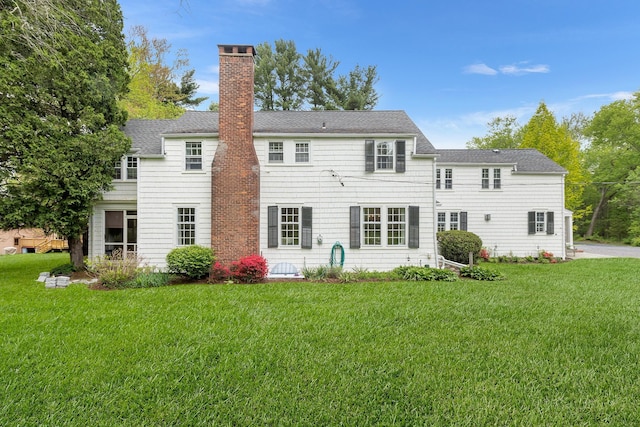 rear view of house featuring a chimney, a yard, and a shingled roof