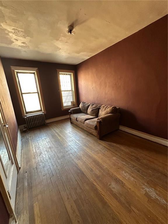 86-03 102nd St Unit 2D, Richmond Hill, NY 11418 - unfurnished living room with hardwood / wood-style floors, radiator heating unit, and baseboards