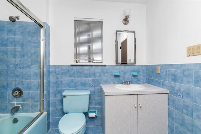 full bath featuring wainscoting, vanity, toilet, tile walls, and bath / shower combo with glass door