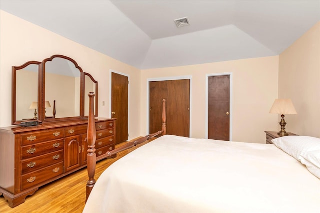 bedroom featuring lofted ceiling, light wood-type flooring, two closets, and visible vents