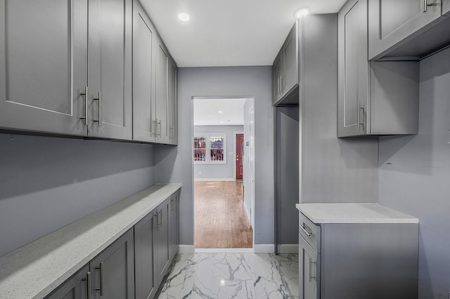 interior space featuring baseboards, light countertops, gray cabinetry, and marble finish floor
