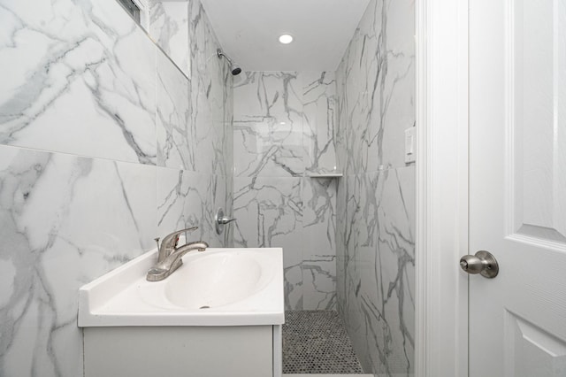 bathroom featuring vanity, a marble finish shower, and tile walls