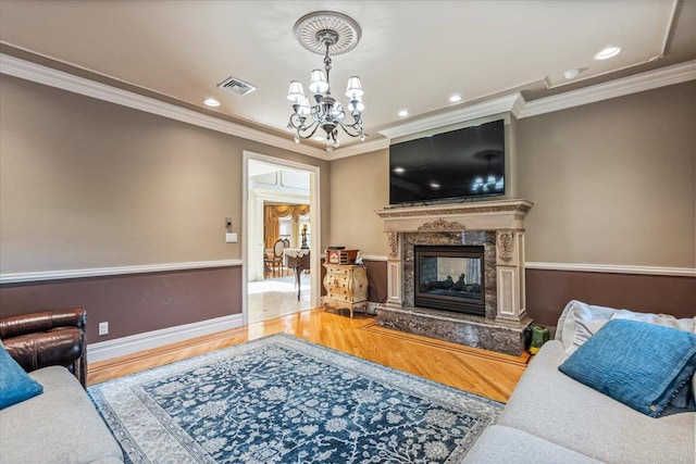 living area with an inviting chandelier, ornamental molding, wood finished floors, baseboards, and a high end fireplace
