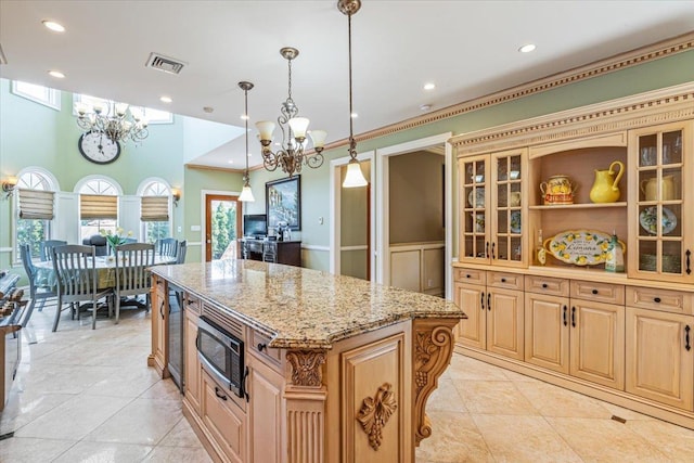 kitchen featuring an inviting chandelier, visible vents, a center island, stainless steel microwave, and light stone counters