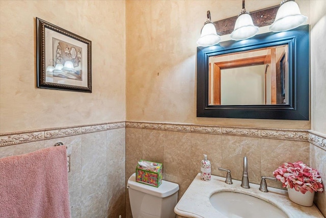 half bathroom featuring vanity, wainscoting, toilet, and tile walls